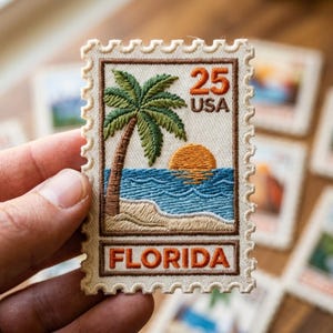 May include: Embroidered patch in the shape of a postage stamp featuring a Florida beach scene with a palm tree, ocean, and setting sun. The patch reads "25 USA" and "FLORIDA" in brown lettering, with a cream-colored border.