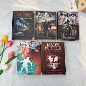 May include: A collection of five hardcover books with the title "James Potter" by G. Norman Lippert. The book covers feature illustrations of characters and scenes, with titles such as "The Hall of Elders' Crossing" and "Crimson Thread."