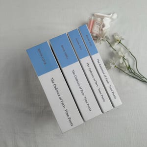Pode incluir: Quatro livros intitulados "The Cadence of Part-Time Poets" est&atilde;o dispostos na diagonal. Cada livro tem uma lombada branca com a parte superior azul e o n&uacute;mero do livro. Um pequeno frasco de perfume e flores brancas est&atilde;o no fundo.