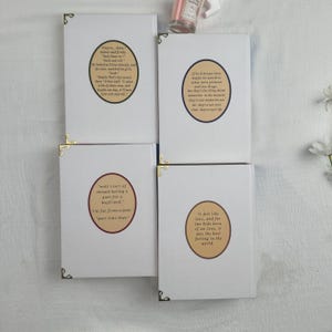 Pode incluir: Quatro cadernos brancos com cantos dourados. Cada caderno apresenta uma cita&ccedil;&atilde;o em um design circular. As cita&ccedil;&otilde;es est&atilde;o em fonte marrom. Os cadernos est&atilde;o dispostos em uma superf&iacute;cie branca.