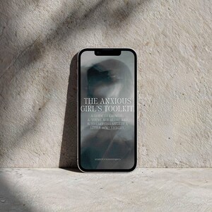 Op de afbeelding: Een smartphone met een digitale cover getiteld THE ANXIOUS GIRL'S TOOLKIT. A GUIDE TO KNOWING A) YOU'RE NOT ALONE AND B) TO CARRYING ANXIETY A LITTLE MORE LIGHTLY. De onderste tekst luidt ANXIETY UNANONYMOUS tegen een donkere, wazige achtergrond.