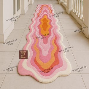 Könnte beinhalten: Ein wellenförmiger, farbenfroher Teppich mit Retro-Design. Der Teppich hat Schichten aus Rosa, Orange und Creme. Der Teppich liegt auf einem gefliesten Boden. Der Text "What The Rug Shop" ist sichtbar.