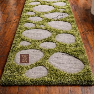 May include: A green and gray area rug with a stone path design. The rug features oval-shaped gray stones set in a field of green, shaggy material. The rug is rectangular and designed for a hallway or entryway.