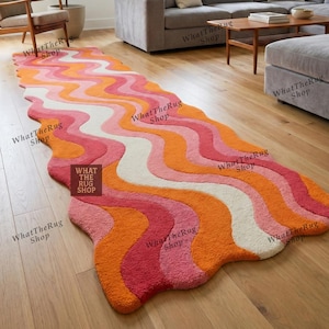 May include: A vibrant, patterned rug with a flowing, wave-like design in orange, pink, and white. The rug is placed on a wooden floor. The text "WHAT THE RUG SHOP" is visible on the rug. The rug's shape is irregular.