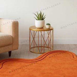 May include: An orange rug with a wavy design on the floor. A gold side table with a geometric base holds two potted plants. A beige sofa is on the left. The room has a minimalist design.