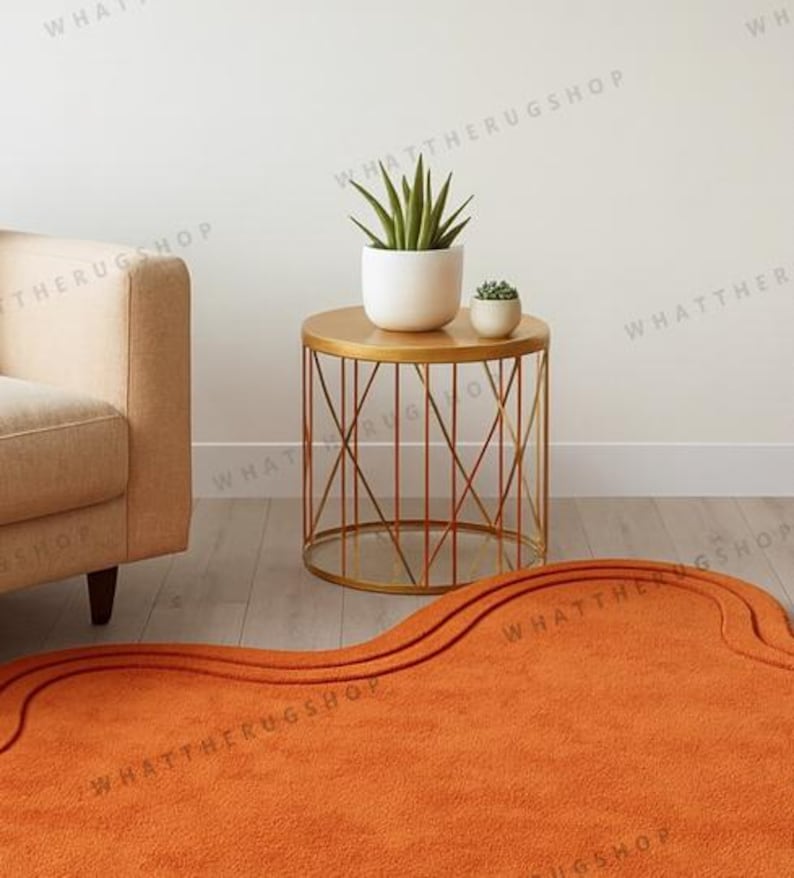 May include: An orange rug with a wavy design on the floor. A gold side table with a geometric base holds two potted plants. A beige sofa is on the left. The room has a minimalist design.