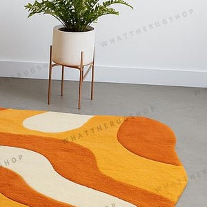 以下が含まれることがあります： オレンジ、黄色、クリーム色のレトロスタイルのラグで、波模様が特徴です。緑の植物が入った白い植木鉢が、銅色のスタンドの上にあります。このラグは部屋に彩りを添えます。