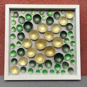 Puede incluir: Una pieza de arte de pared enmarcada que presenta un mosaico de círculos verdes y dorados dispuestos en un patrón geométrico.