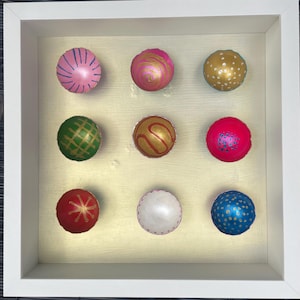 May include: Nine round, painted, decorative bowls in a white frame. The bowls are arranged in three rows of three. The bowls are painted in various colours and patterns, including pink, green, red, blue, and gold.