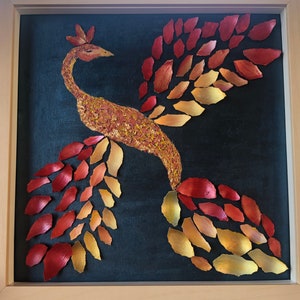 Puede incluir: Una obra de arte enmarcada que representa un fénix estilizado hecho de piezas de hojas rojas y doradas sobre un fondo negro.