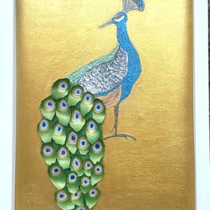 Puede incluir: Obra de arte enmarcada con una ilustración de un pavo real. El pavo real está representado con plumaje azul y verde sobre un fondo dorado. La obra de arte está encerrada en un marco blanco, añadiendo una estética limpia y moderna a la pieza.