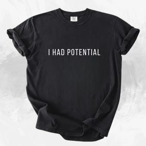 May include: Black t-shirt with the white text "I HAD POTENTIAL". The shirt has short sleeves and a crew neck. The fabric appears to be soft and slightly wrinkled.