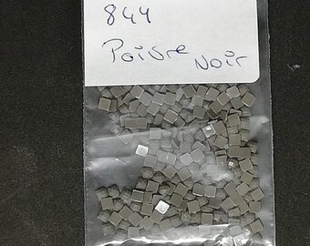 May include: A clear plastic bag containing a large quantity of small, square, gray beads. A white label on the bag reads "844 Poivre Noir".