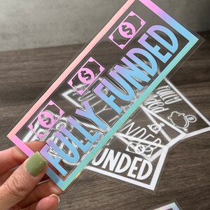 Puede incluir: Una pegatina rectangular con un borde hologr&aacute;fico y el texto "FULLY FUNDED" en letras grandes y negritas. El dise&ntilde;o incluye peque&ntilde;os iconos de billetes de d&oacute;lar con el s&iacute;mbolo de d&oacute;lar. La pegatina tiene un fondo transparente y un acabado reflectante.