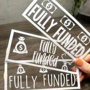 Puede incluir: Tres calcoman&iacute;as rectangulares de vinilo blanco perla con el texto "FULLY FUNDED" en varias fuentes. Los dise&ntilde;os incluyen iconos de billetes, bolsas de dinero y una alcanc&iacute;a. Estos adhesivos tienen un acabado iridiscente sutil.