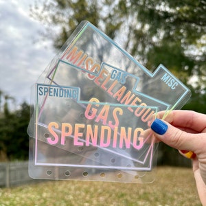 May include: Three clear plastic binder dividers with iridescent borders and text. The dividers feature labels including MISCELLANEOUS, GAS, MISC, and SPENDING printed in a gradient color scheme. Each divider has a row of holes along the bottom edge.