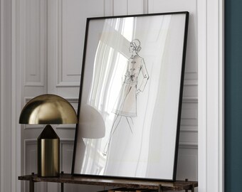May include: A black framed print of a line drawing of a woman wearing a dress and coat. The print is hanging on a wall above a shelf with books and a lamp. The shelf is made of wood and has a black metal frame.