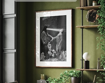 May include: A black and white photograph of two people in a forest setting. The photo is framed in a dark wood frame and hanging on a green wall. The wall is also decorated with a shelf with plants and a lamp.