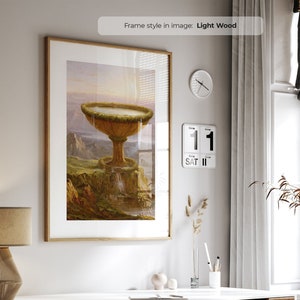 May include: A framed print of a painting depicting a large, golden chalice-like structure with a waterfall flowing from it. The chalice is surrounded by lush greenery and a rocky landscape. The painting is set against a backdrop of a cloudy sky.