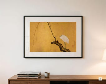 May include: A framed wall art print featuring a white heron perched on a dark, gnarled tree branch against a solid gold background. The artwork includes thin, delicate branches extending upward and a small red seal mark on the right side of the print.