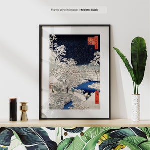 May include: A framed print of a Japanese woodblock print depicting a snowy landscape with a bridge and figures. The print is in black, white, and shades of blue. The frame is black.