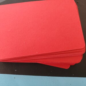 May include: A stack of red cardstock paper. The paper is smooth and has a slight sheen.