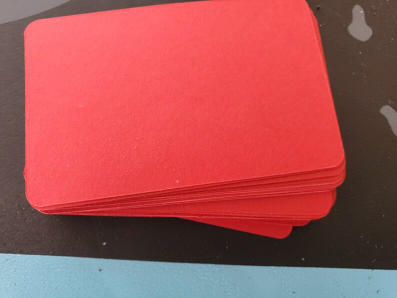 May include: A stack of red cardstock paper. The paper is smooth and has a slight sheen.