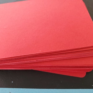 May include: A stack of red cardstock paper. The paper is smooth and has a slight sheen.