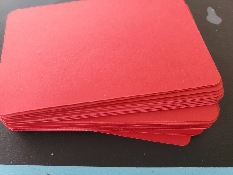 May include: A stack of red cardstock paper. The paper is smooth and has a slight sheen.