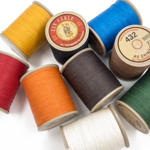 May include: Assortment of spools of thread in various colours, including red, orange, yellow, brown, blue, green, and white. Each spool is labelled "Lin Cable Au Chinois Ets Toulemonde Successeurs" and has a number printed on it.