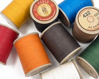 May include: Assortment of spools of thread in various colors, including red, orange, yellow, brown, blue, green, and white. Each spool is labeled "Lin Cable Au Chinois Ets Toulemonde Successeurs" and has a number printed on it.