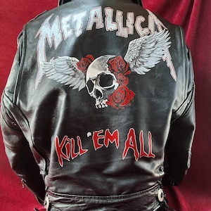 Op de afbeelding: Zwarte leren jas met een geschilderd ontwerp op de rug. Het ontwerp bevat het woord "METALLICA" in het wit, een schedel met vleugels en rozen, en de woorden "KILL 'EM ALL" in het rood.