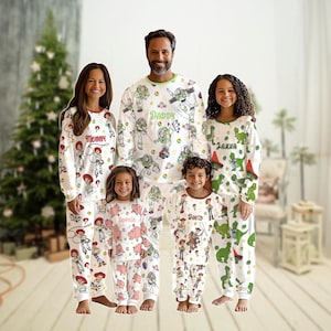 May include: A family in matching white Toy Story pyjamas. The pyjamas feature long sleeves and trousers. The text "Mommy", "Daddy", "Janna", "David", and "Sophia" is printed on the pyjamas. A Christmas tree is visible in the background.