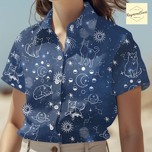 May include: A blue short-sleeved button-down shirt with a white print of cats, stars, moons, and celestial bodies.