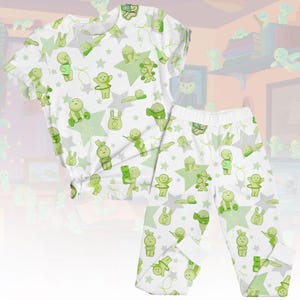 Könnte beinhalten: Weißes Pyjama-Set mit einem sich wiederholenden Muster aus grünen Cartoon-Figuren, Sternen und anderen Formen. Das Set enthält ein kurzärmeliges Oberteil und eine Hose. Das Pyjama-Set ist aus einem weichen, bequemen Material.