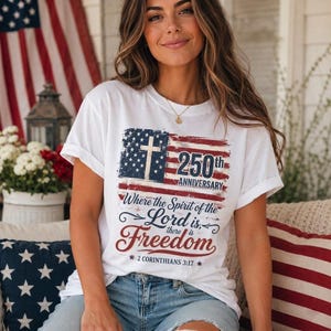 Könnte beinhalten: Ein weißes Kurzarm-T-Shirt mit einer Grafik der amerikanischen Flagge im Used-Look, einem Kreuz, dem Text 250th ANNIVERSARY und dem Zitat Where the Spirit of the Lord is, there is Freedom, gefolgt von der Angabe 2 CORINTHIANS 3:17.