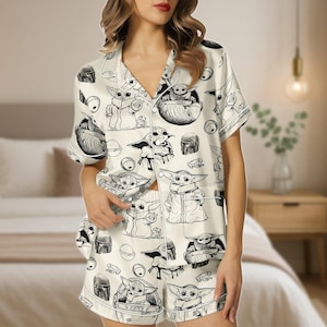 Può includere: Pigiama color crema con un'illustrazione in bianco e nero di un personaggio di una popolare serie di fantascienza. Il set include una camicia abbottonata a maniche corte e pantaloncini abbinati. Il pigiama ha finiture bianche.