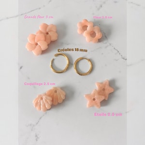 May include: A collection of jewelry pieces, including earrings and charms, in a soft peach color. The image features two gold-colored hoop earrings, flower-shaped charms (3 cm), shell-shaped charms (2.5 cm), and star-shaped charms (2.5 cm). The text "Créoles 18 mm" is visible.