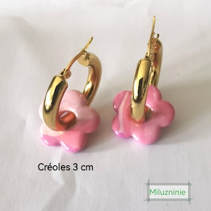 May include: Gold-coloured hoop earrings with pink flower-shaped charms. The earrings are 3 cm in diameter. The flower charms have a marbled effect with shades of pink and white.