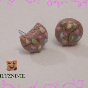 Puede incluir: Un par de pendientes de galleta de color marrón y rosa con chispas de colores. Los pendientes están hechos de arcilla polimérica y tienen forma de galleta.