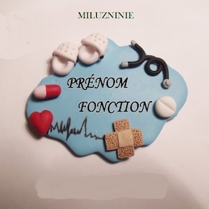 Puede incluir: Insignia de arcilla azul y blanca con un estetoscopio, píldoras, una venda, un corazón y una línea de latido del corazón. La insignia dice "PRÉNOM FONCTION" en texto negro.