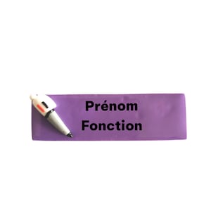 Könnte beinhalten: Ein lila Namensschild mit den Worten "Prénom Fonction" in schwarzer Schrift. Ein kleiner stiftförmiger Gegenstand ist auf der linken Seite des Schildes befestigt. Der Stift ist weiß, grau und schwarz.