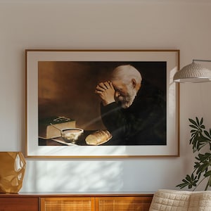 Op de afbeelding: Een ingelijst kunstwerk met een biddende man hangt boven een houten kast in het midden van de eeuw. Een beige fauteuil en een vloerlamp met een geweven kap staan ​​in de buurt. Een decoratieve vaas en een tapijt maken de inrichting van de kamer compleet.