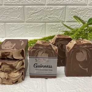 Op de afbeelding: Drie bruine en beige gemarmerde zeepjes met een label met de tekst "Guinness Extra Stout Beer Soap Handcrafted Soap".
