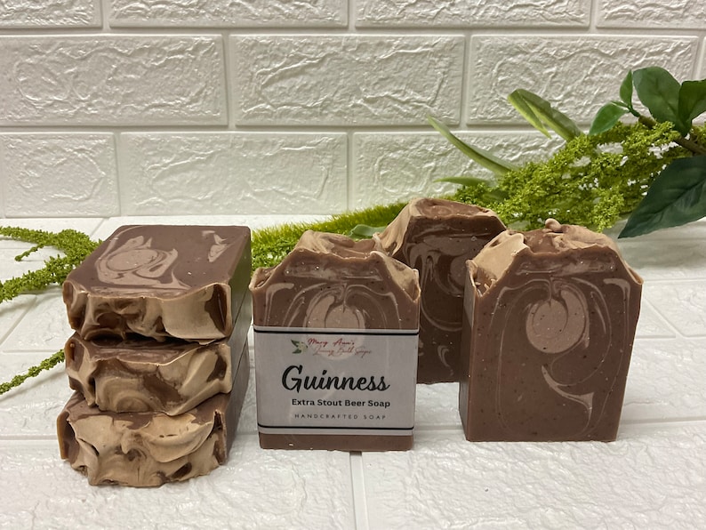 Op de afbeelding: Drie bruine en beige gemarmerde zeepjes met een label met de tekst "Guinness Extra Stout Beer Soap Handcrafted Soap".