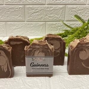 Op de afbeelding: Zes bruine en witte gemarmerde zeepjes met een label met de tekst "Guinness Extra Stout Beer Soap Handcrafted Soap".