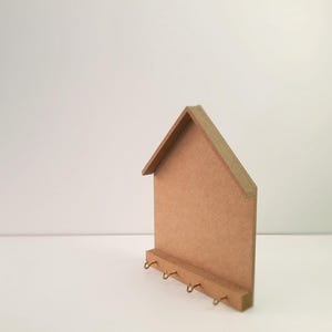 May include: A wooden house-shaped key holder with five hooks. The key holder is made of light brown wood and has a simple design.