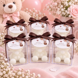 May include: Six clear square boxes containing white bear-shaped candles, each topped with a dark brown ribbon and a circular tag featuring a hot air balloon illustration, a heart, and the text Sofia Baby Shower in a clean, sans-serif font.