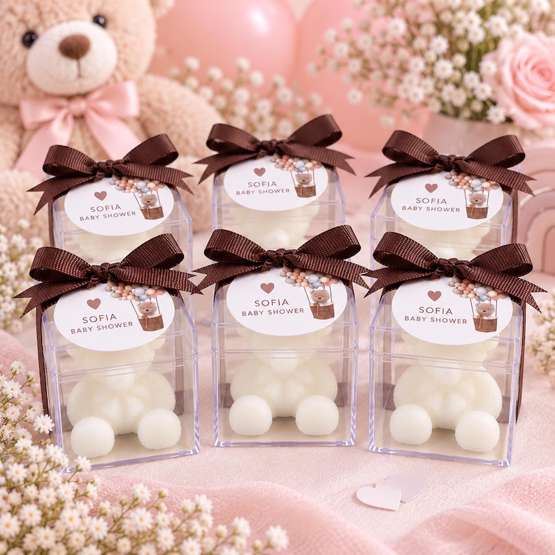 May include: Six clear square boxes containing white bear-shaped candles, each topped with a dark brown ribbon and a circular tag featuring a hot air balloon illustration, a heart, and the text Sofia Baby Shower in a clean, sans-serif font.