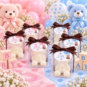 May include: Clear square boxes containing white teddy bear-shaped soaps, each topped with a brown ribbon and a personalized tag. Tags feature either the name Sofia with pink balloons or Liam with blue balloons and the text Baby Birthday.